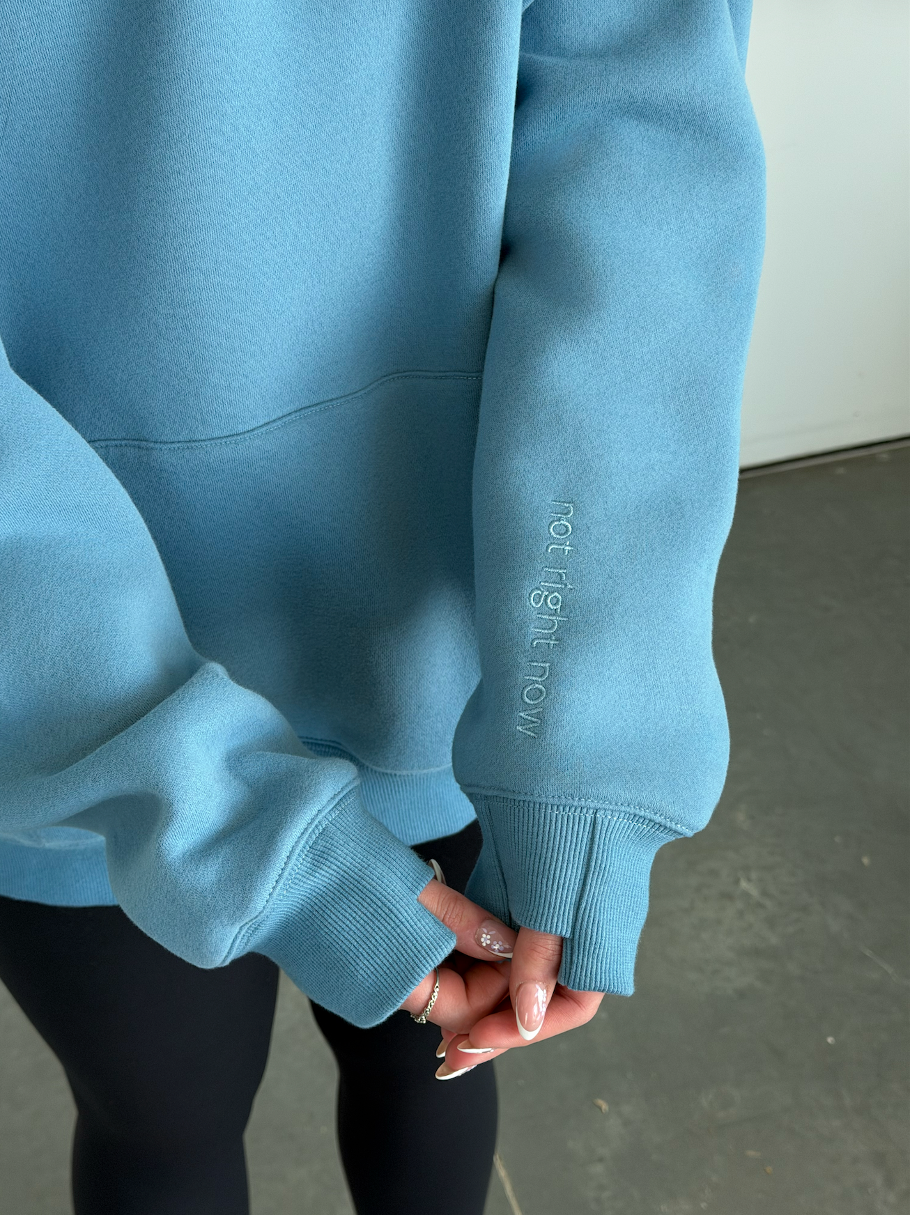Light blue sweatshirt with text on sleeve held by a person against a neutral background