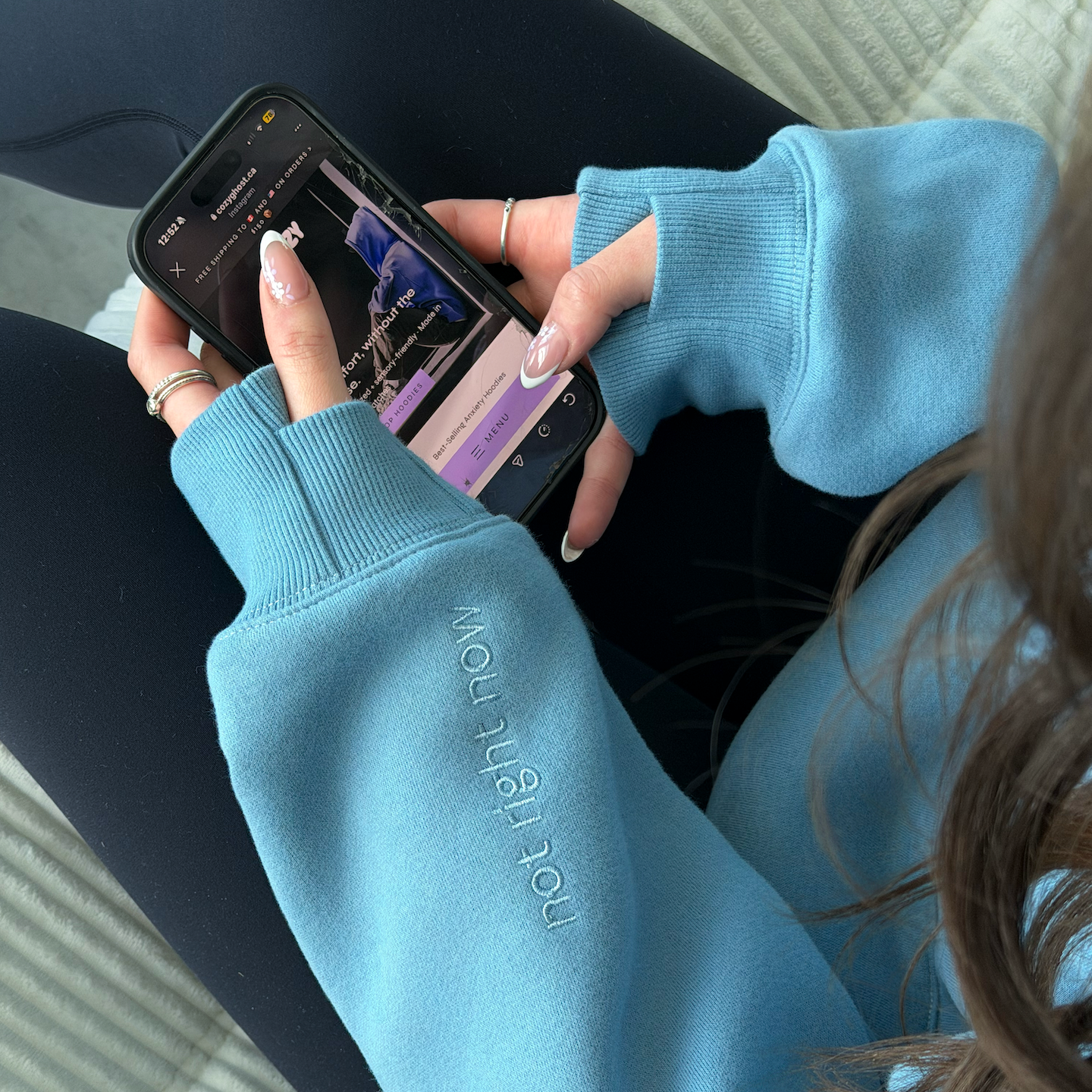 Person wearing a blue sweater with text, using a smartphone on a textured surface.