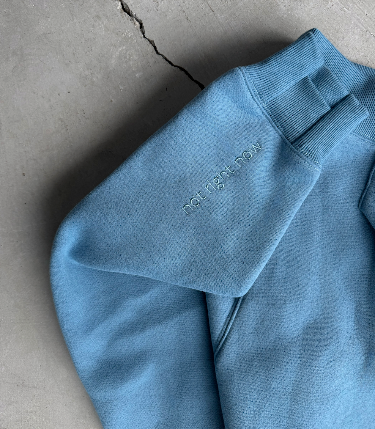 Blue sweatshirt with 'Right Now' text on a concrete surface