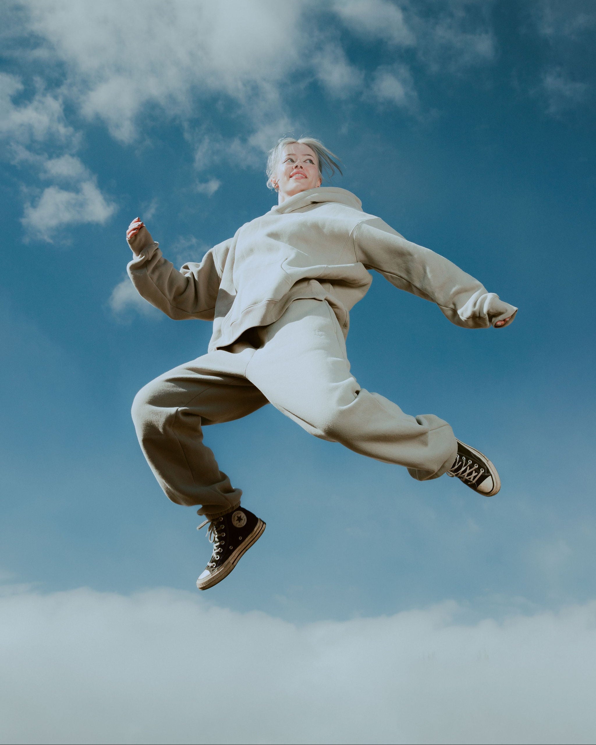 Person in beige jacket and pants jumping against a blue sky with clouds