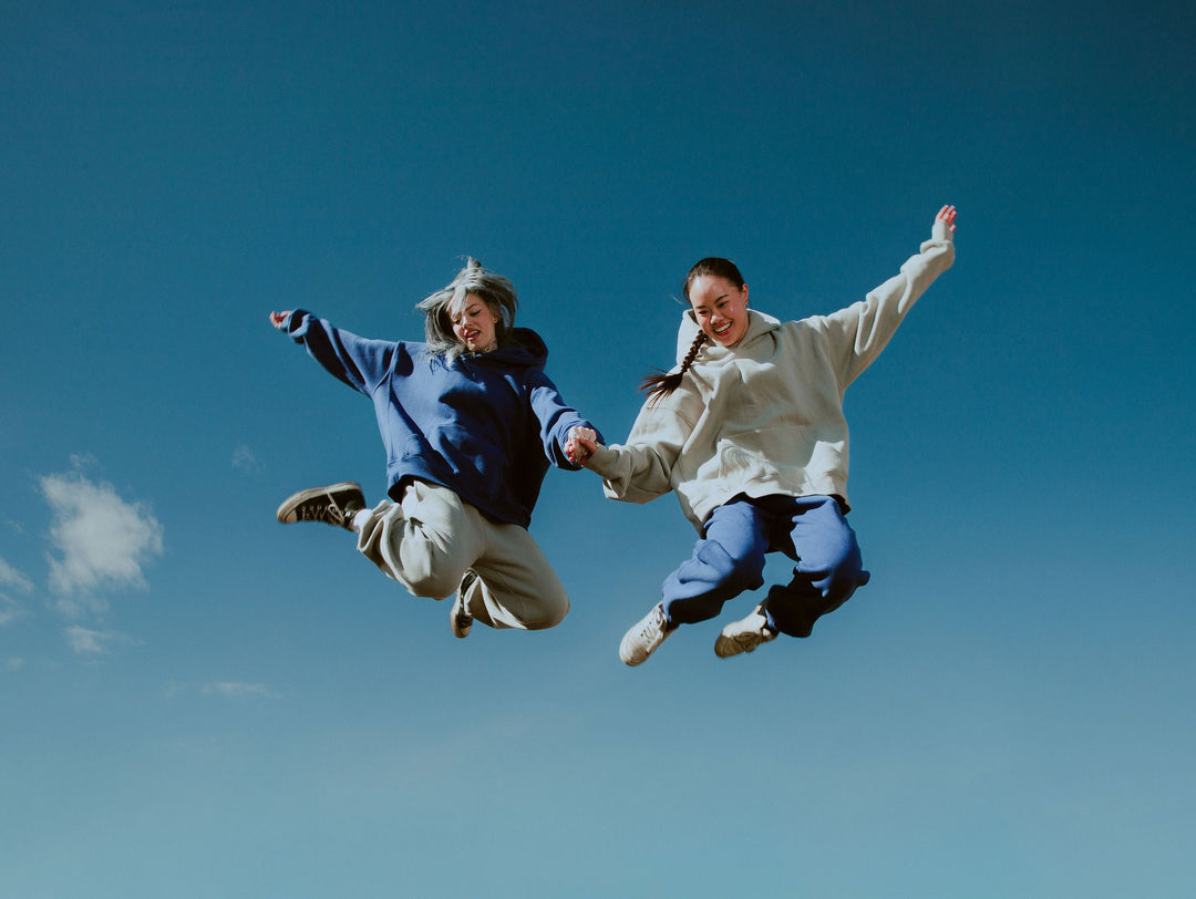 Two people jumping against a clear blue sky