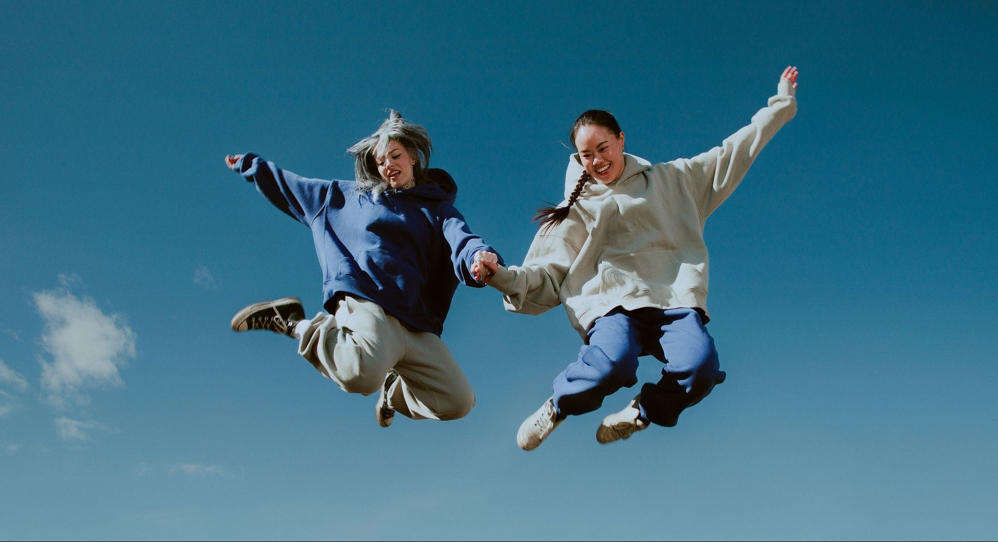 Two people jumping against a clear blue sky