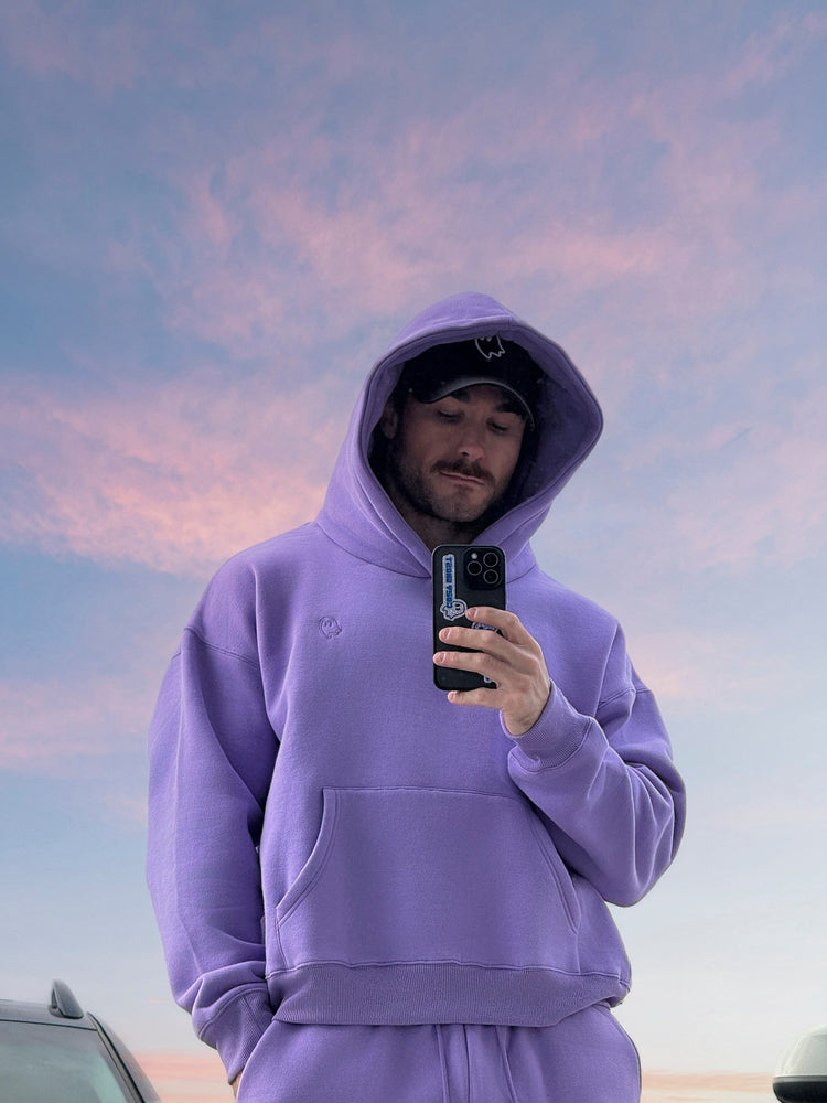 Person wearing a purple hoodie taking a selfie against a colorful sky.